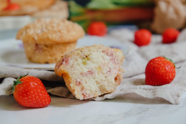 Aufgeschnittener Rhabarber-Erdbeer-Muffin mit Kokos. Daneben liegen frische Erdbeeren.